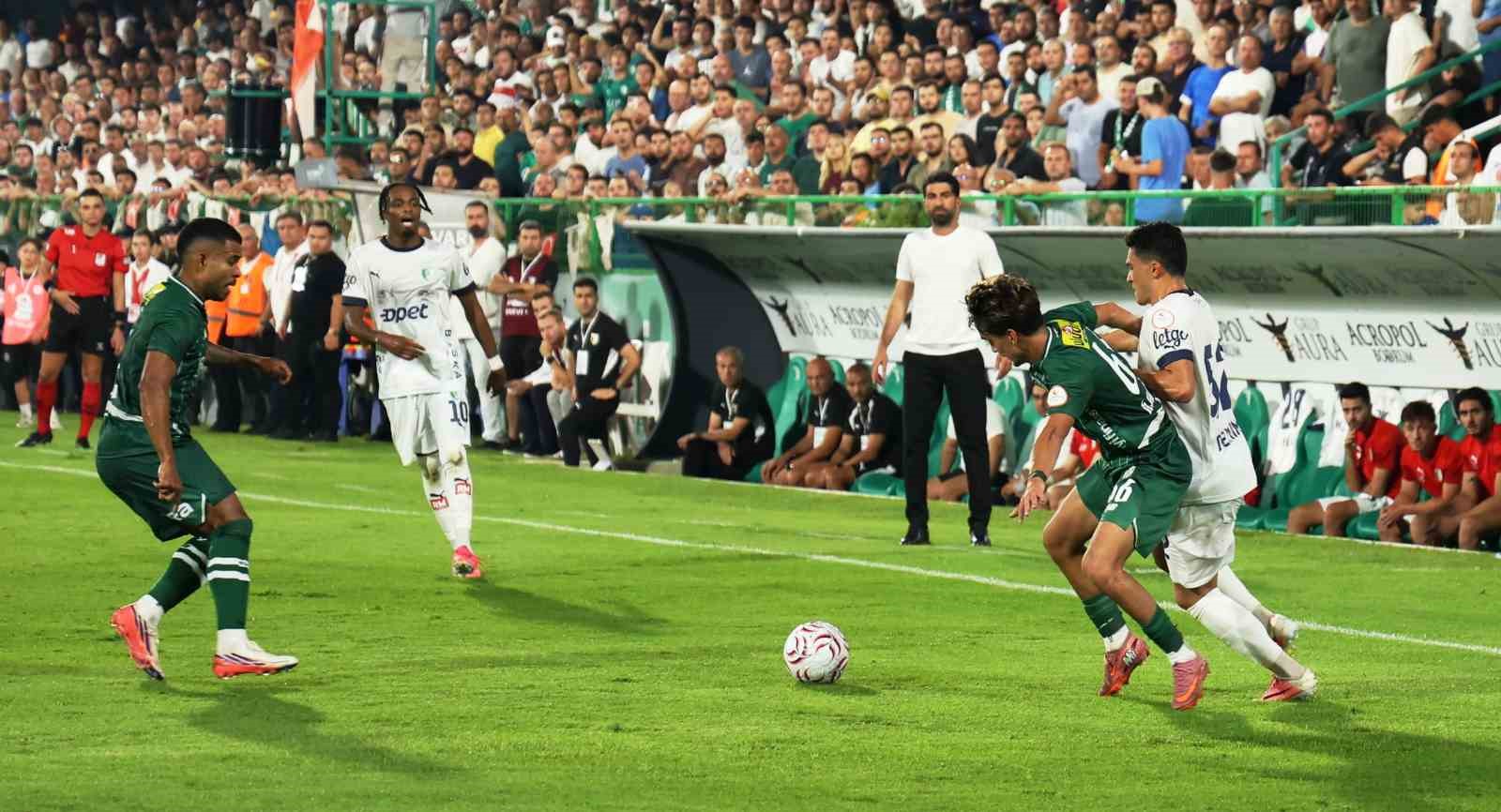 Taç çizgisi yakınında top için mücadele eden futbolcular ve tribünler.