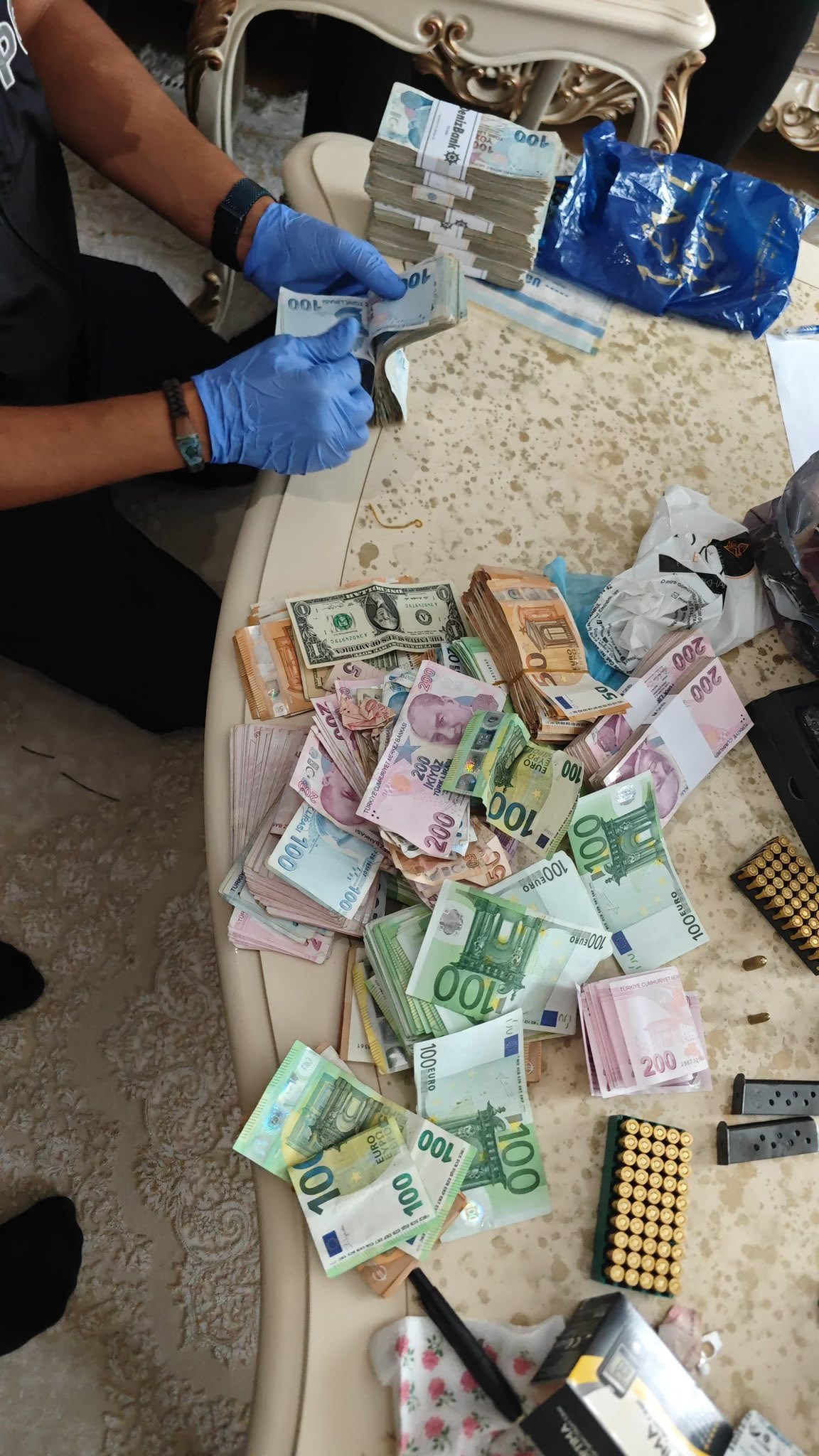 Bir masada farklı para birimlerinden banknotlar, mermiler ve şarjörlerin bulunduğu görüntü.