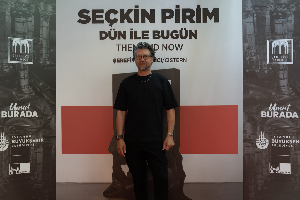 Seçkin Pirim’in “Dün ile Bugün” sergisi tanıtım alanı önünde sanatçının portresi.