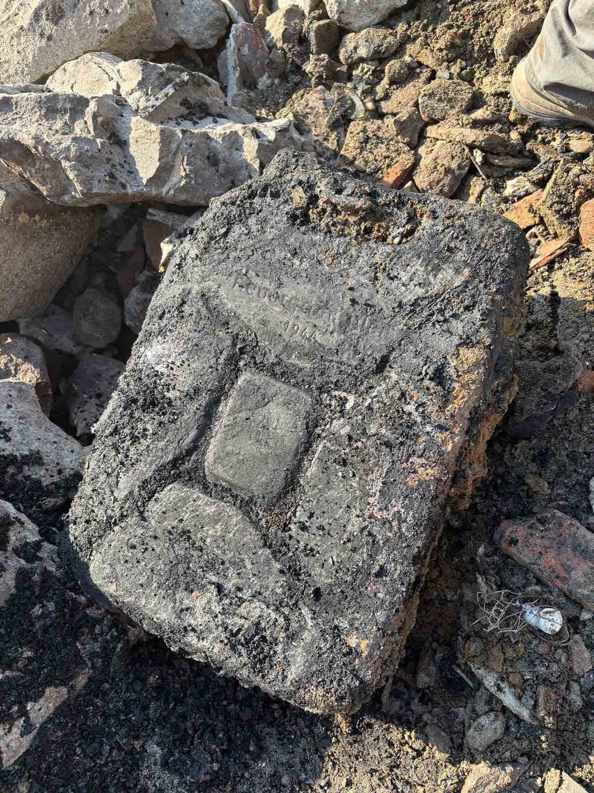 Tuna kıyısında bulunan, üzerinde yazı izleri görülen savaş döneminden kalma yıpranmış metal veya taş parça.