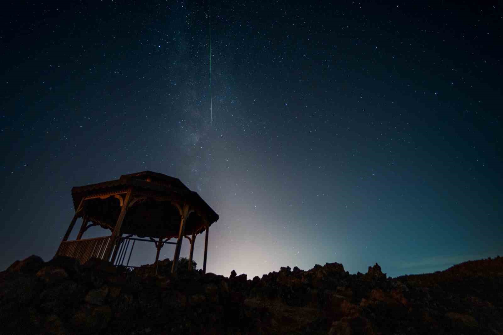 Kula’da karanlık gökyüzünde dikey bir meteor izi ve volkanik arazi silüeti.