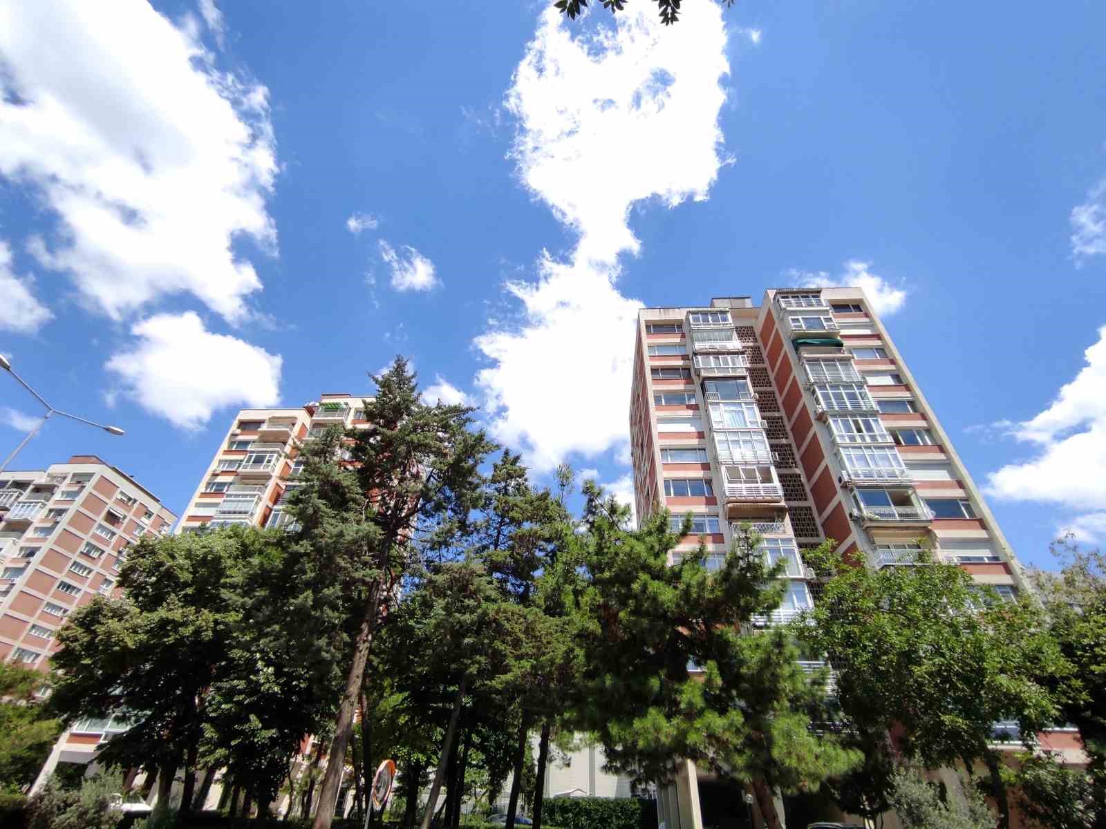 Ağaçların arkasında yükselen apartman blokları ve açık gökyüzü.