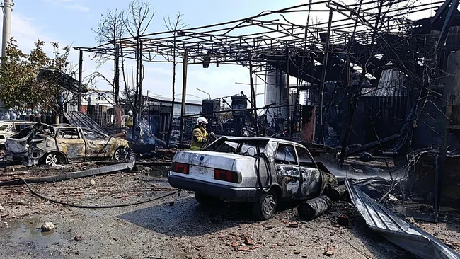 Patlama sonrası gaz dolum tesisinin çevresinde yanmış araçlar, enkaz ve ekiplerin çalışması.