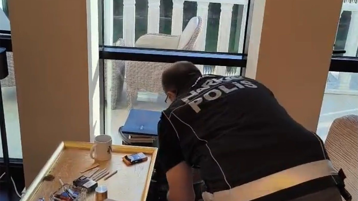 Polis yelekli bir görevlinin iç mekanda arama yaptığı görüntü.