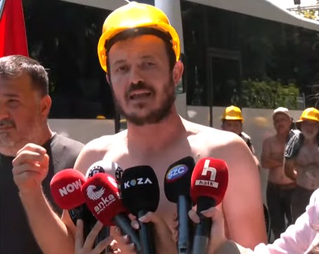 Doruk Madencilik işçisi, sarı baretle eylem alanında mikrofonlara konuşuyor.