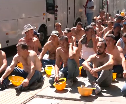 Bakanlık önündeki eylemde sarı baretli maden işçileri kaldırımda oturuyor.