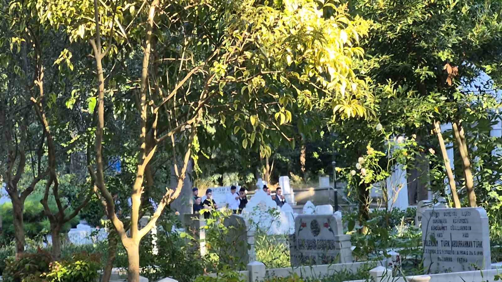 Mezarlık alanında ağaçlar ve mezar taşları arasında toplanan kişiler.