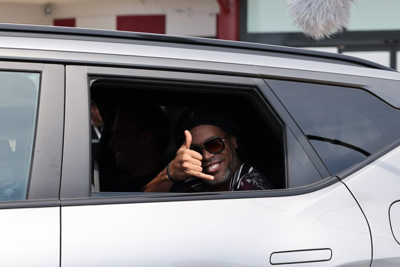 Ronaldinho bir aracın arka koltuğunda gülümseyerek el işareti yapıyor.