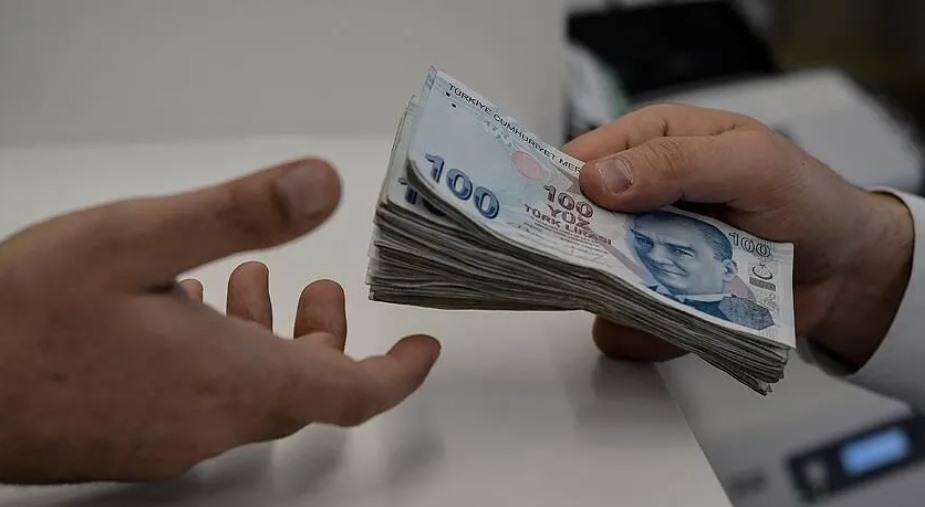 Bir kişinin diğerine deste halinde 100 TL banknot uzattığı görüntü.