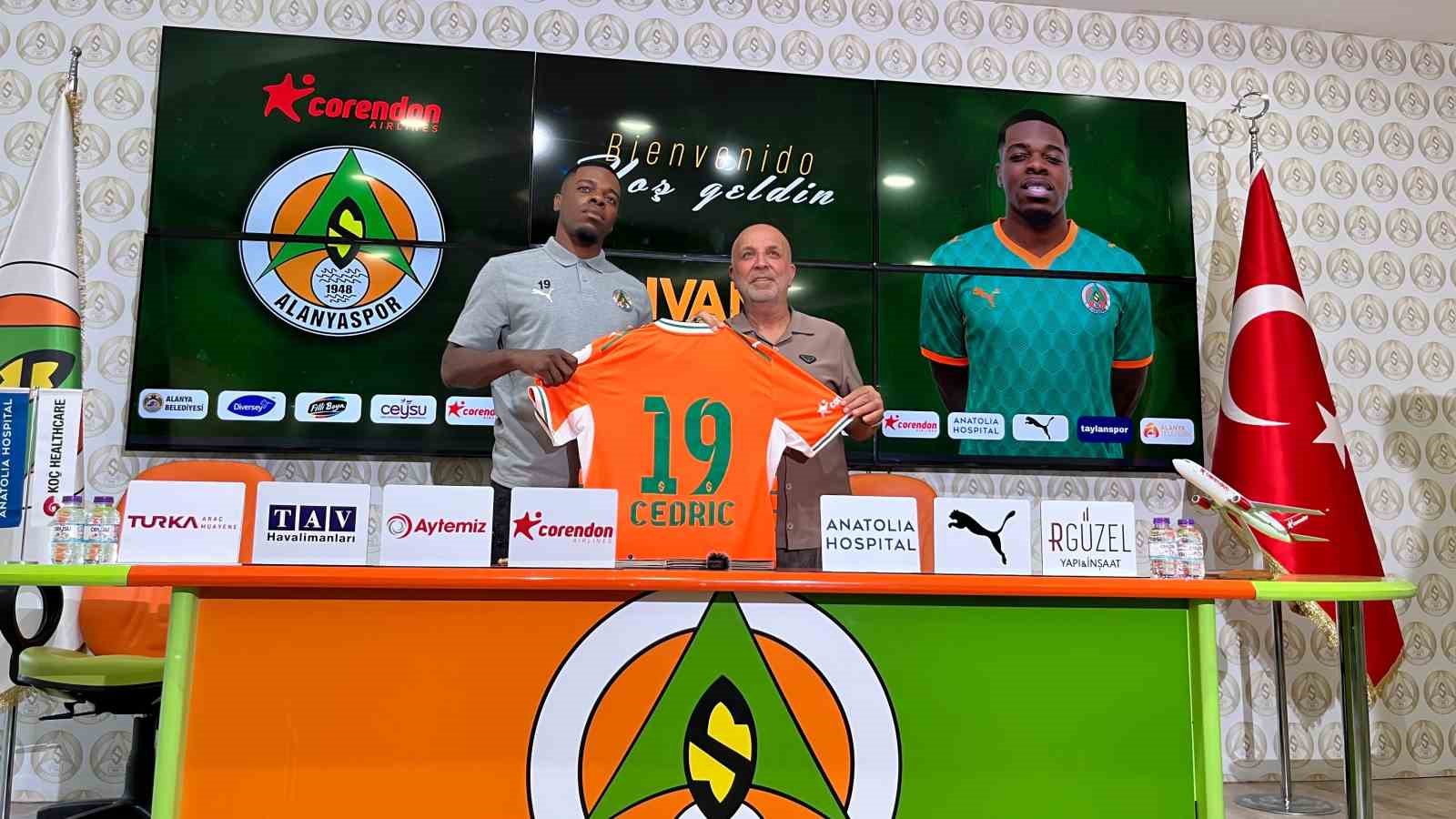 Ivan Cedric ve Alanyaspor Başkanı Hasan Çavuşoğlu, imza töreninde turuncu-yeşilli formayı tutuyor.