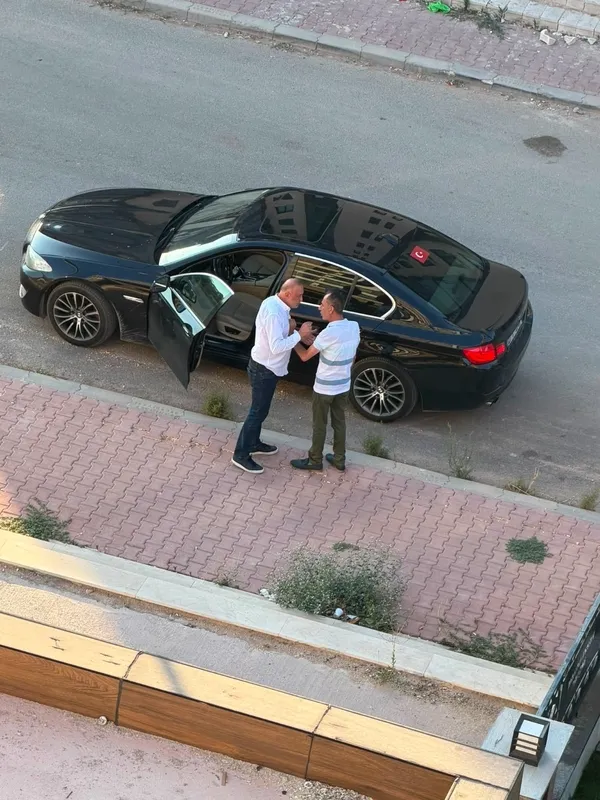 A photo showing two people next to a black vehicle parked on the street.