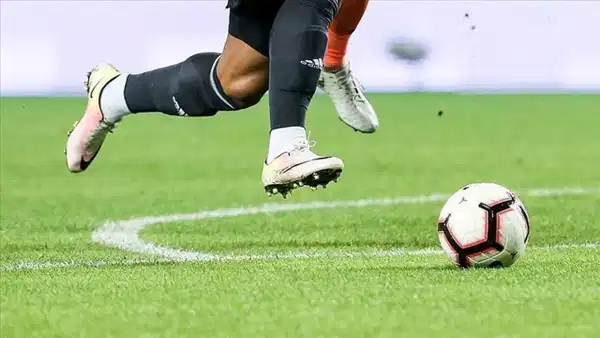 Yeşil sahada futbol topuna doğru koşan futbolcu ayakları.