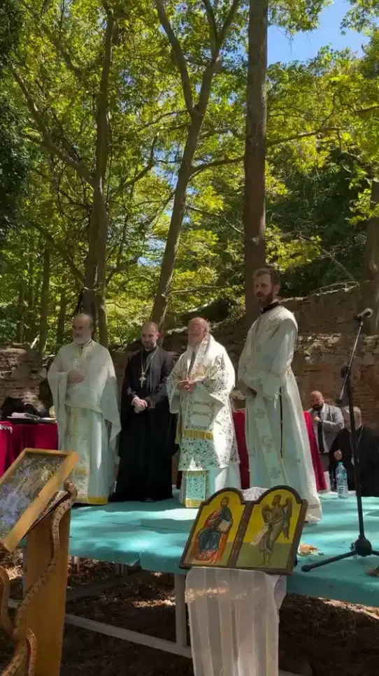 Ağaçlar ve manastır kalıntıları arasında kurulan alanda din görevlilerinin ayine katıldığı görülüyor.