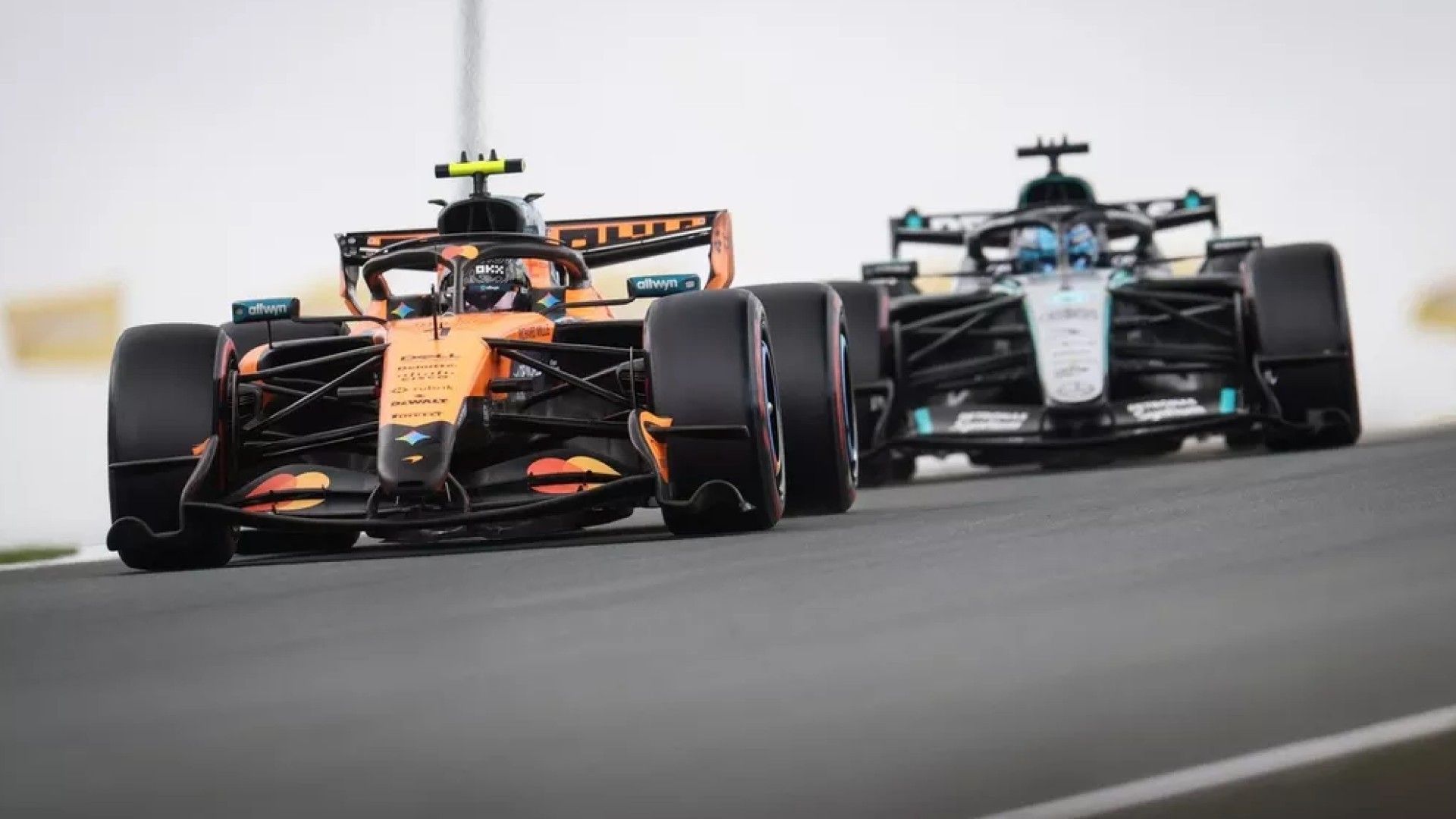 Pistte ilerleyen turuncu McLaren aracı ve arkasındaki Mercedes aracı.