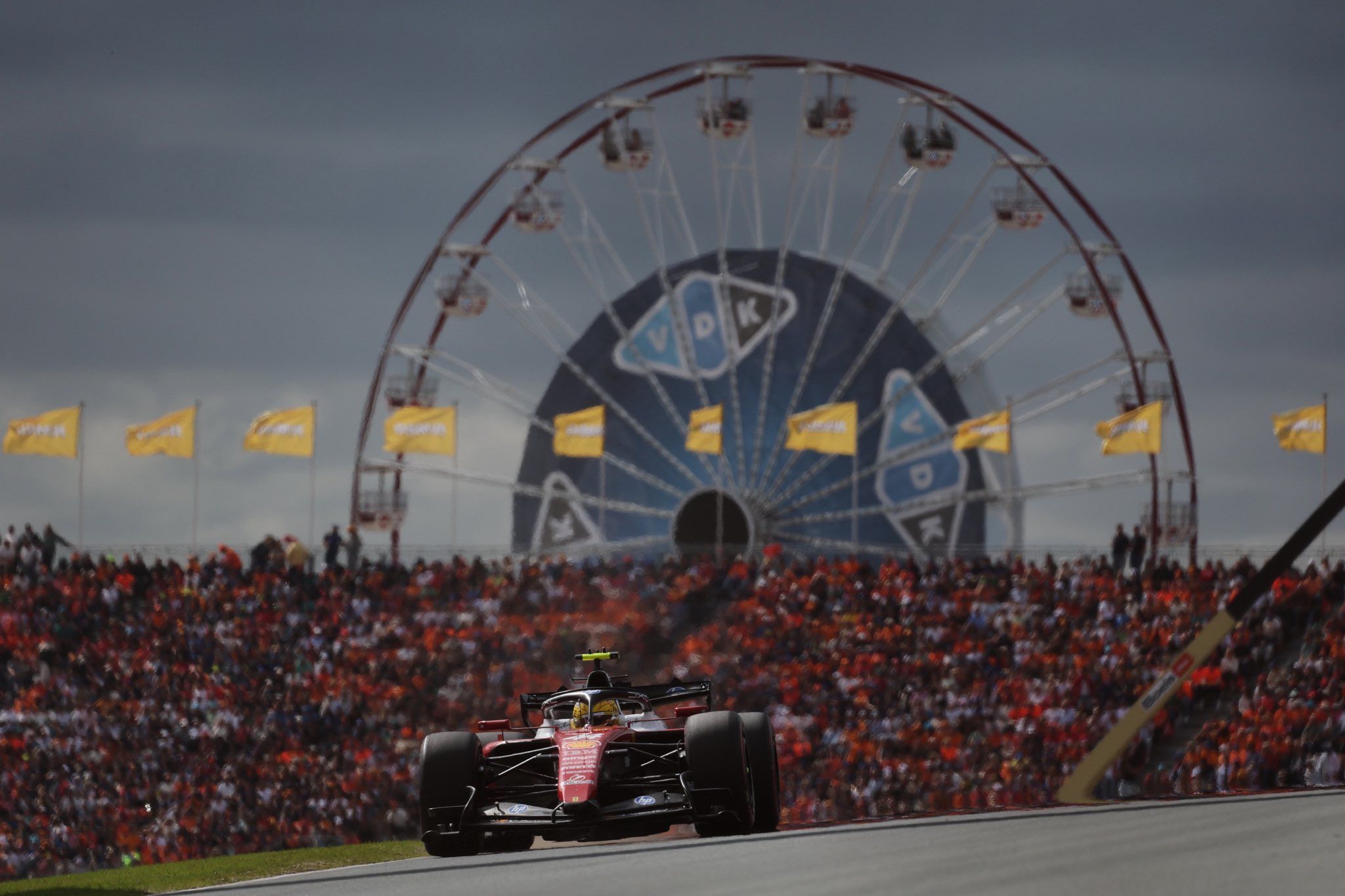 Zandvoort pistinde dönme dolap ve kalabalık tribünler önünden geçen kırmızı Formula 1 aracı.