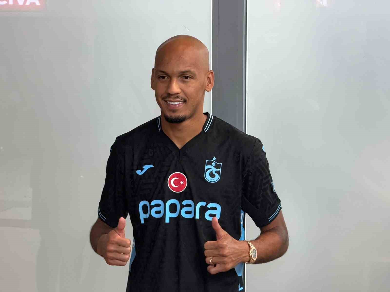 Fabinho, siyah Trabzonspor formasıyla iç mekanda başparmaklarını kaldırarak poz veriyor.