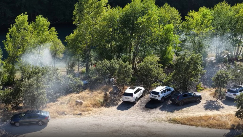 An area where smoke is rising near parked vehicles in a wooded area.