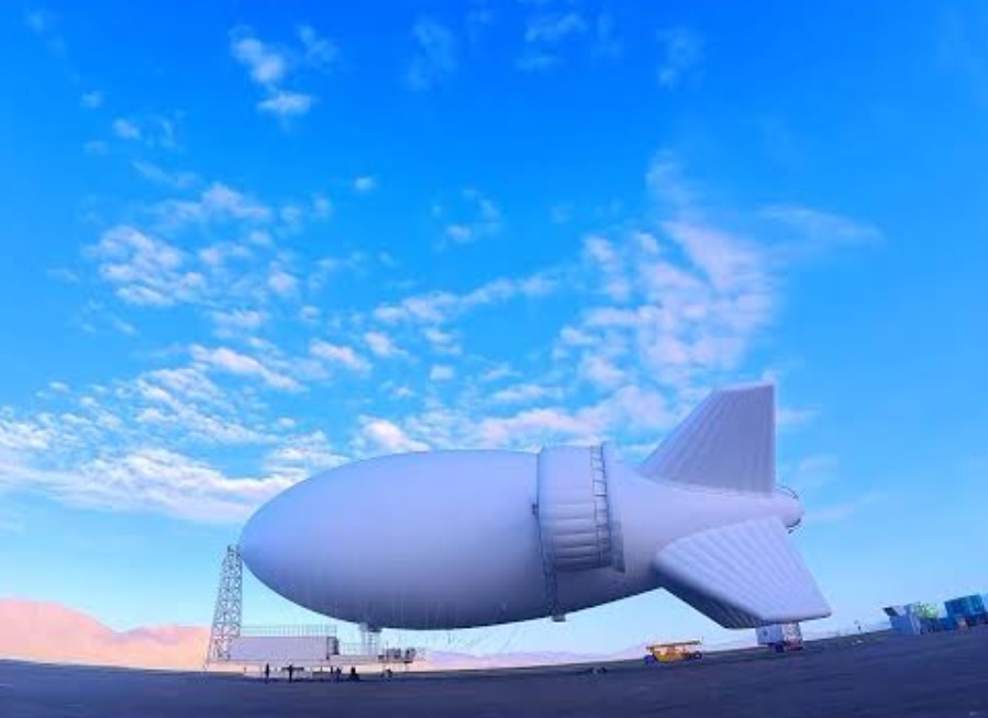 A large white airship-shaped flying wind system being prepared on the ground under a clear sky.