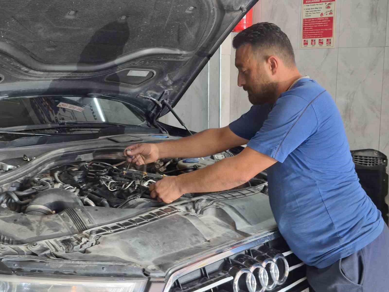 Osman San, servis içinde kaputu açık bir araçta parça kontrolü yapıyor.