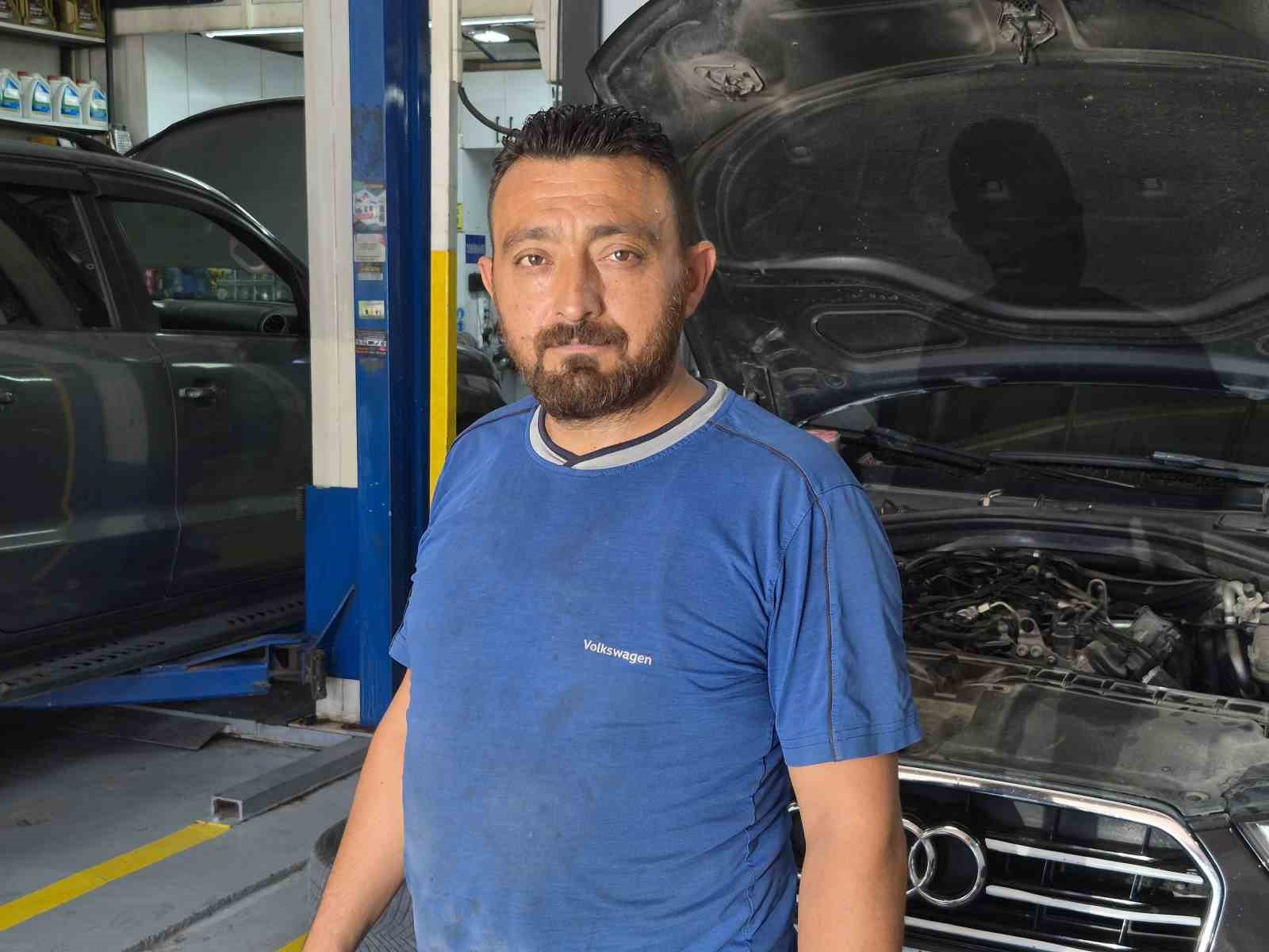 Osman San, servis içinde kaputu açık bir aracın yanında poz veriyor.