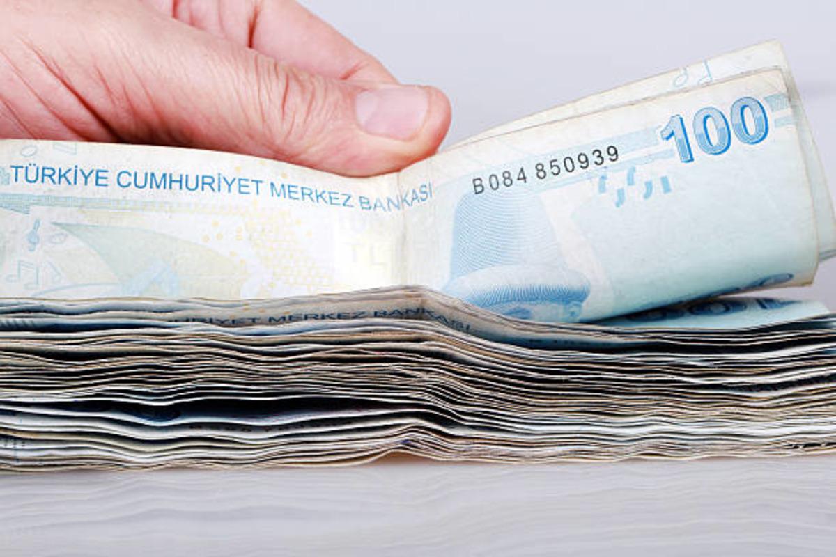 Mazzo di banconote in lire turche e una banconota da 100 lire tenuta in mano.