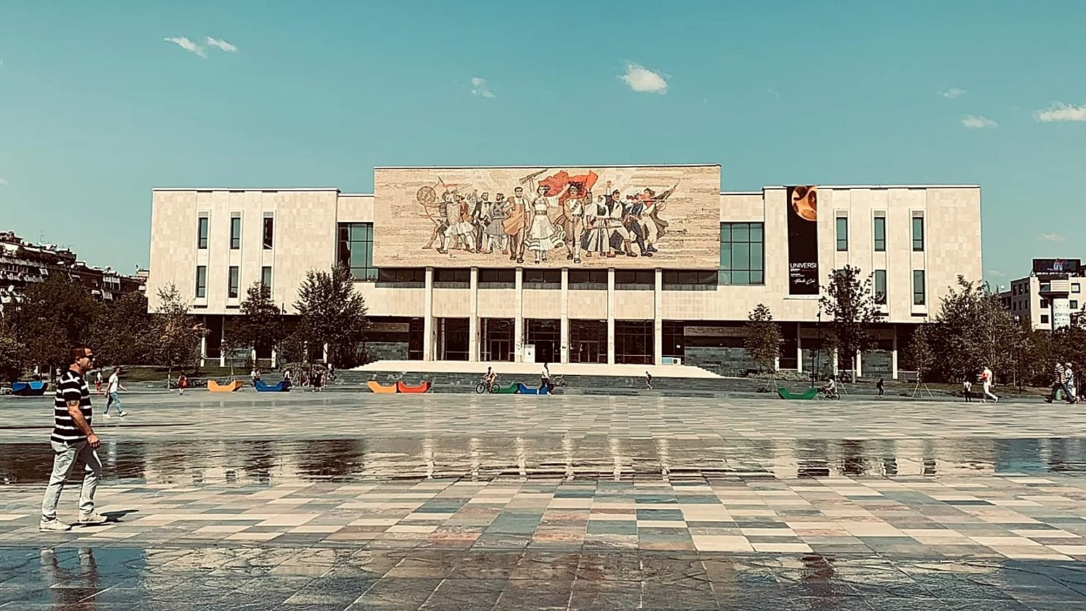 Vue urbaine montrant une large place et un bâtiment public moderne à Tirana.