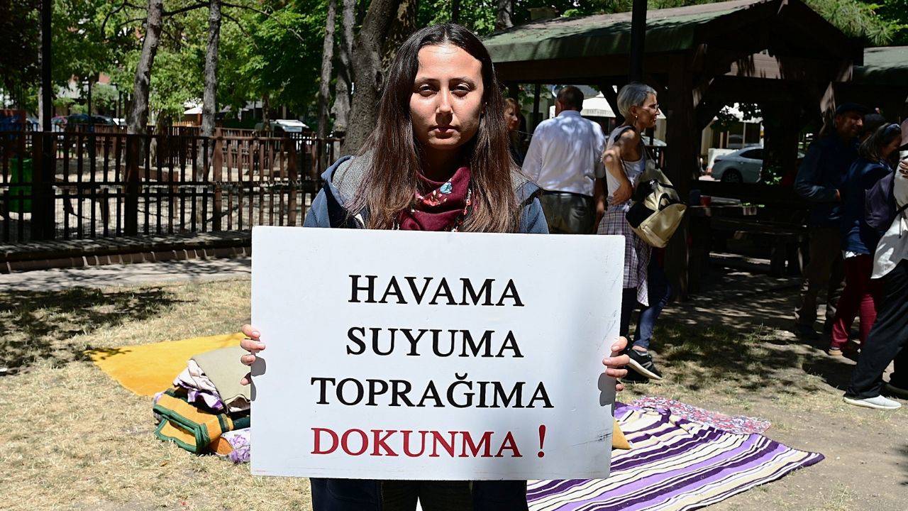 Genç bir kadın, üzerinde 'Havama suyuma toprağıma dokunma' yazan bir döviz tutuyor.