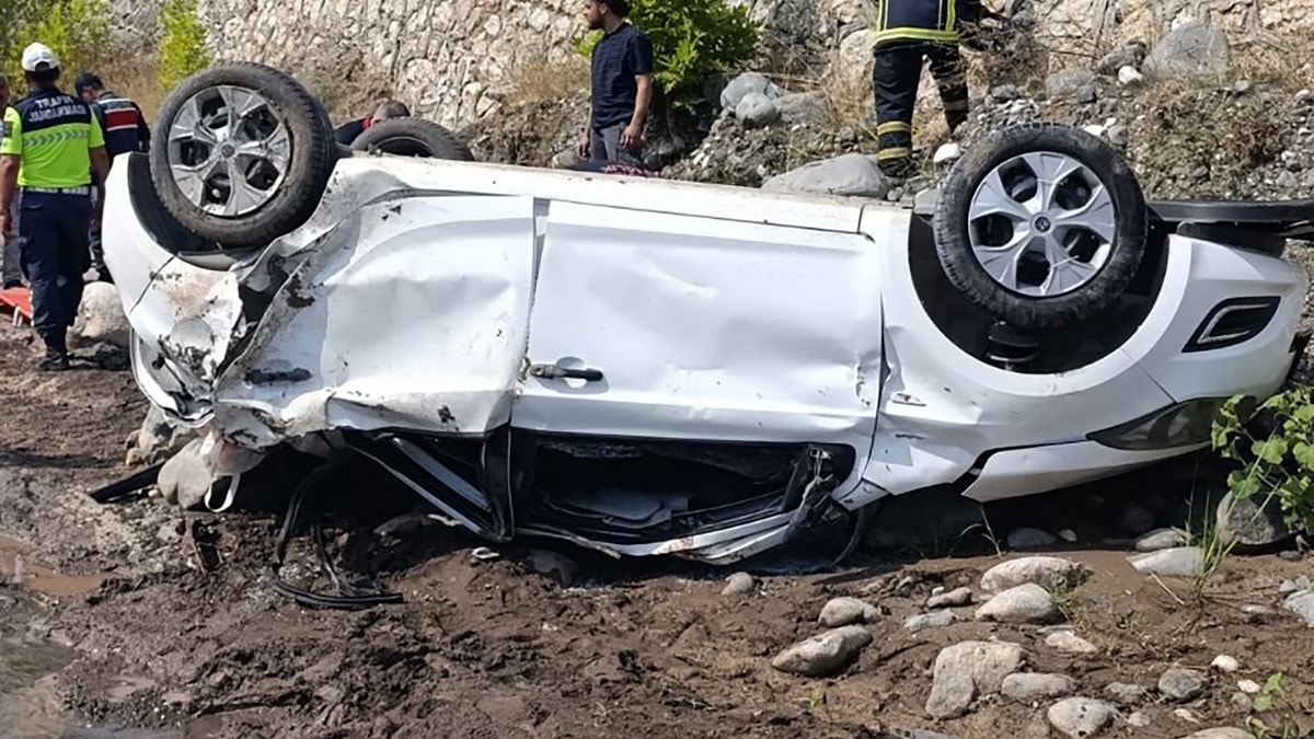 Adana Aladağ’da dereye uçan beyaz otomobilin ters dönmüş hali ve olay yerindeki ekipler.