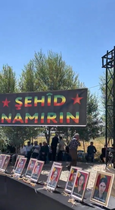 Yüksekova’daki taziye programında üzerinde yazı bulunan pano ve yan yana dizilmiş fotoğraflar görülüyor.