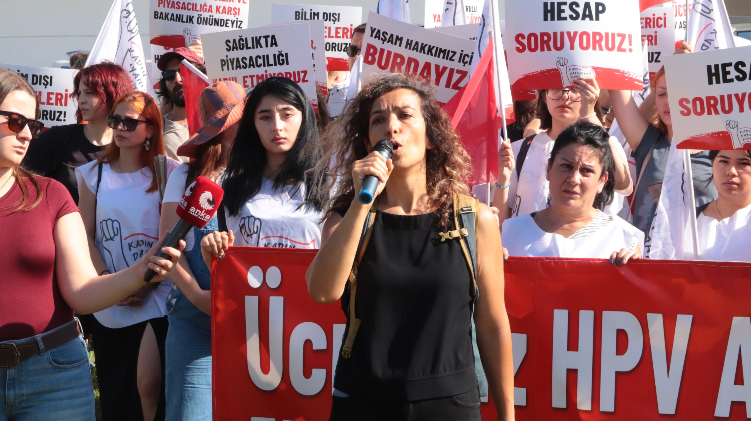 Banu Ünver speaking with a microphone in front of the crowd at the Ministry and the protesters.
