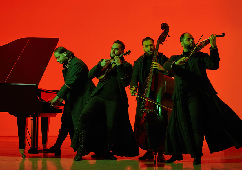 Janoska Ensemble members performing with piano, violin, and double bass in front of a red background.