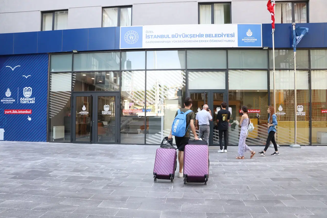 Students waiting with their suitcases at the entrance of an Istanbul Metropolitan Municipality student dormitory.