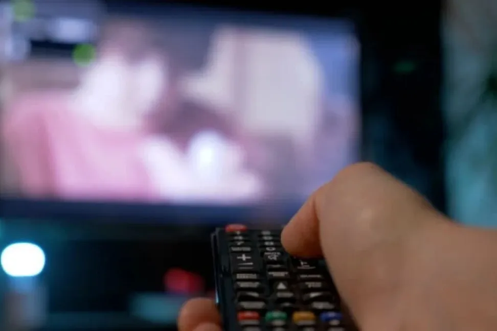 An image of a person watching television holding a remote control.