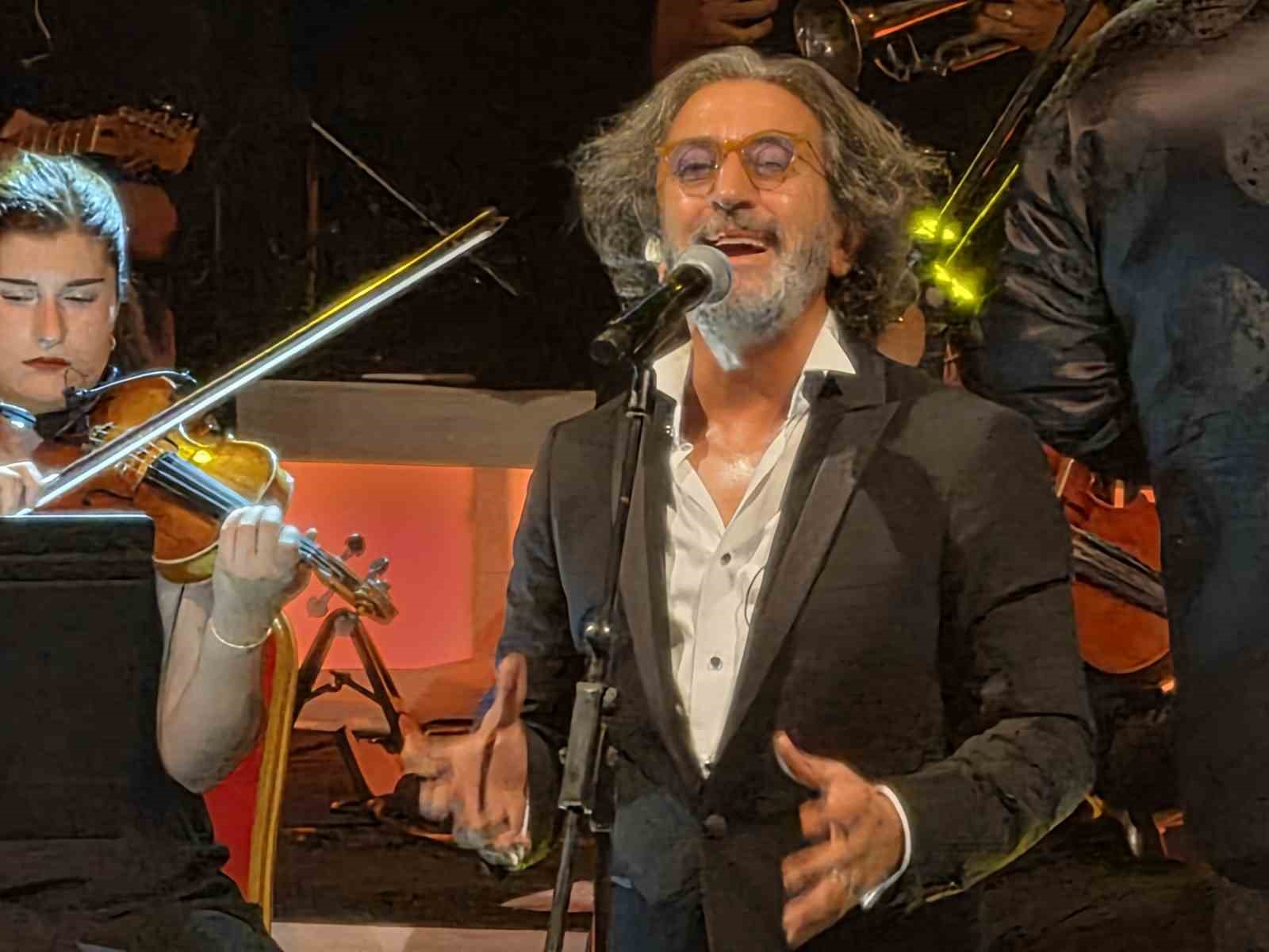 Fettah Can, sahnede mikrofon başında gülümseyerek şarkı söylüyor.
