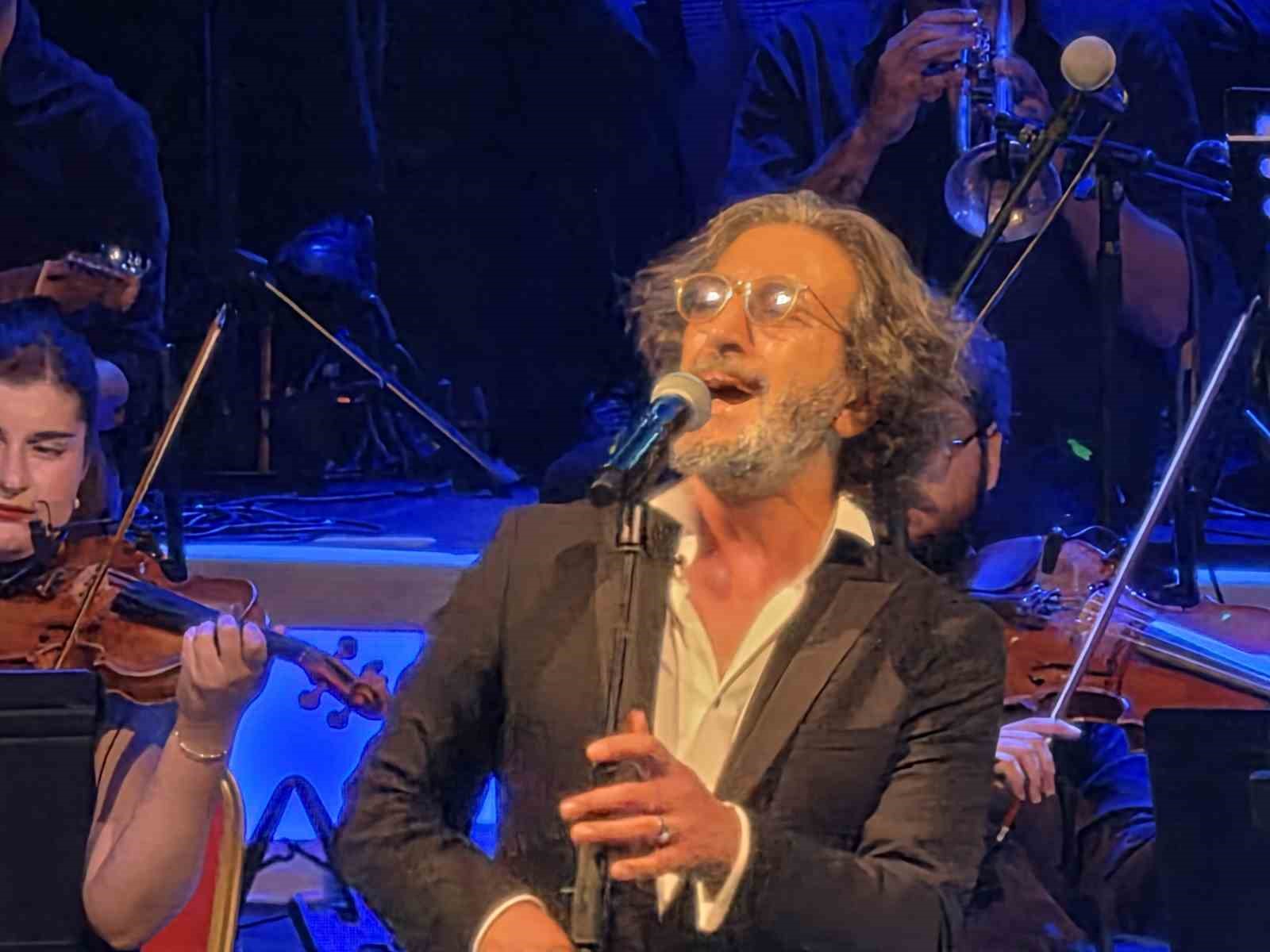 Fettah Can, orkestra eşliğinde mikrofon başında şarkı söylerken görülüyor.