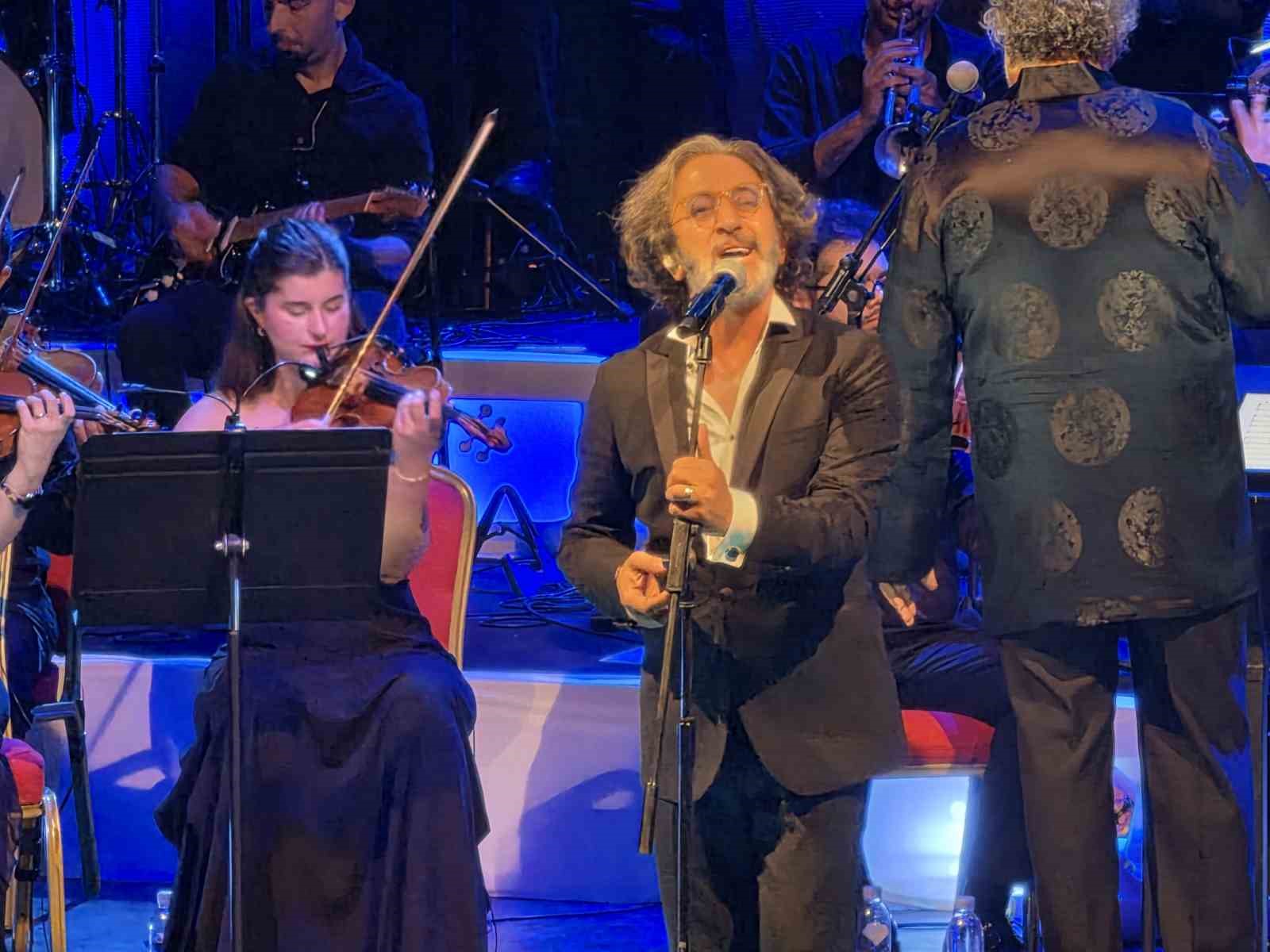 Fettah Can, sahnede mikrofon başında orkestrayla birlikte performansını sürdürüyor.