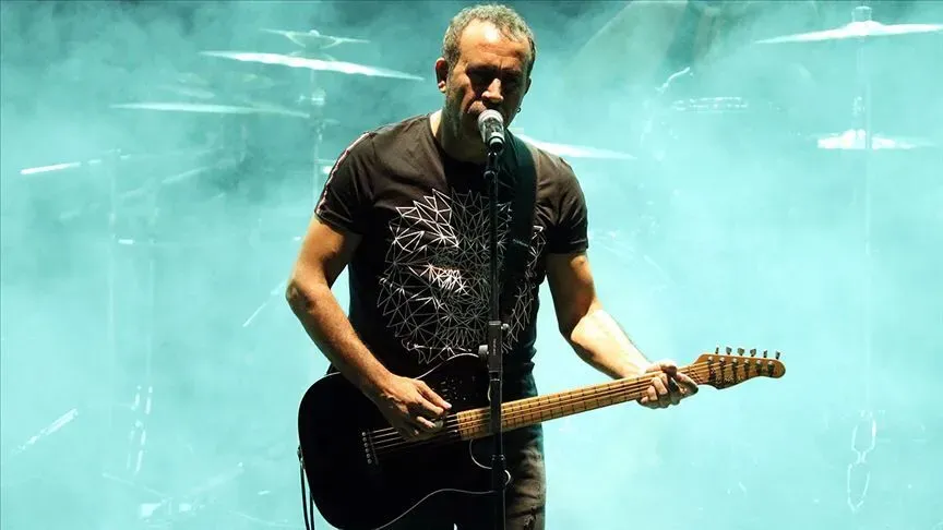 Haluk Levent sahnede gitarıyla mikrofon başında görülüyor.