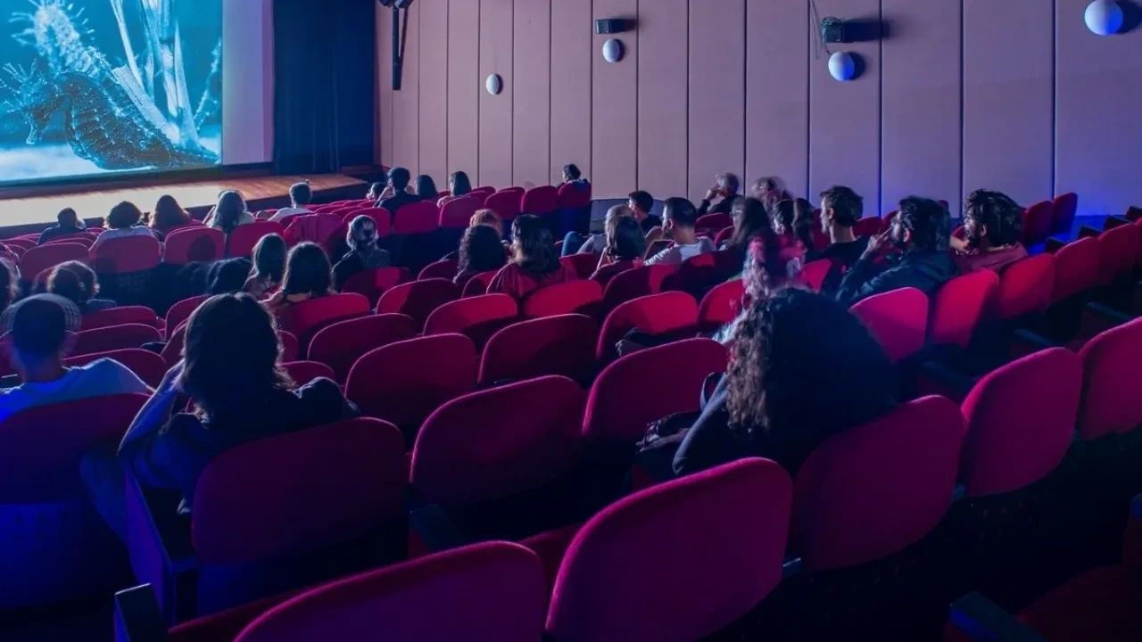 Kırmızı koltuklu bir sinema salonunda film izleyen seyirciler.