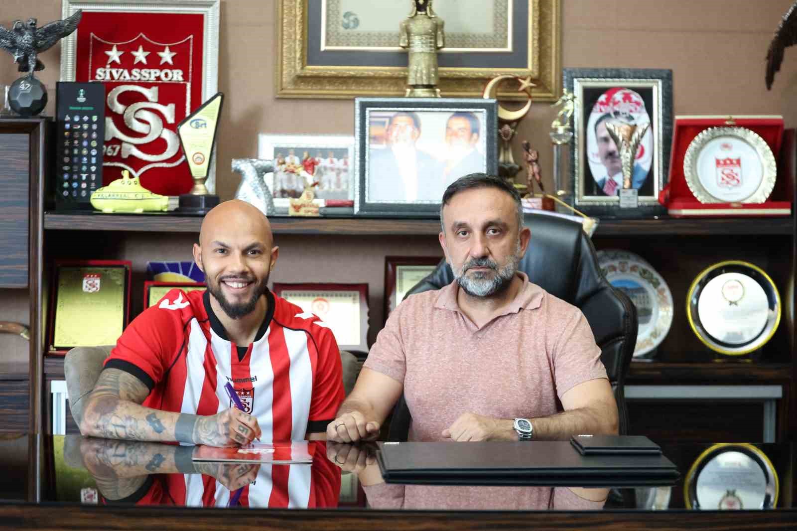 Sivasspor forması giyen futbolcu, kulüp yöneticisiyle imza töreninde görülüyor.