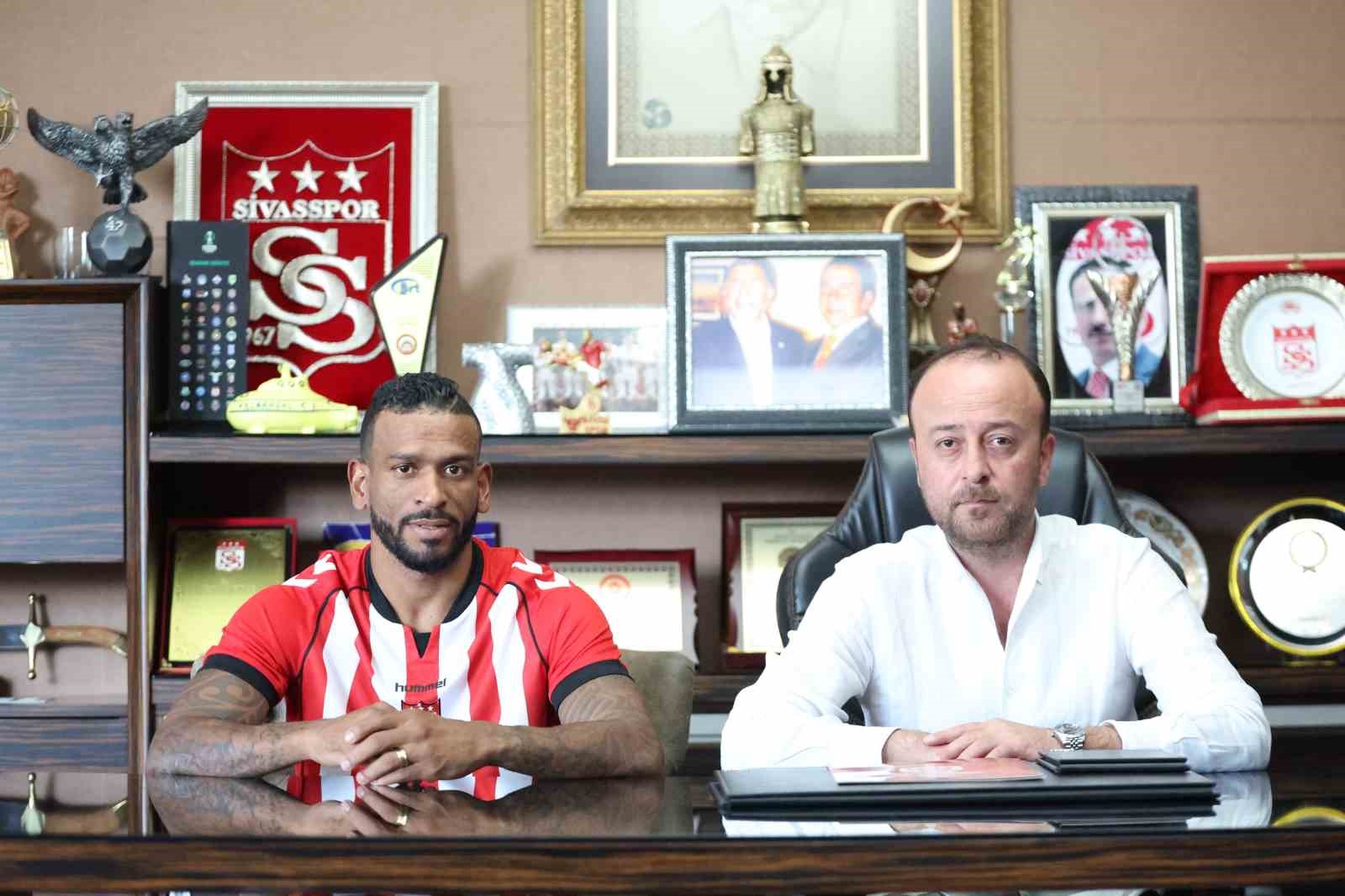 Sivasspor forması giyen futbolcu ve kulüp yöneticisi imza töreninde masada oturuyor.