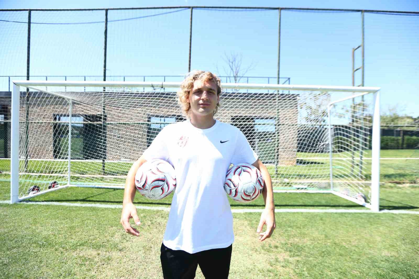 Hamza Akman, futbol sahasında iki topu kollarının altında tutuyor.