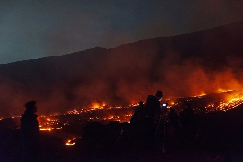Etna Yanardağı çevresinde lav akışını izleyen kişilerin siluetleri ve dumanlı gece manzarası.