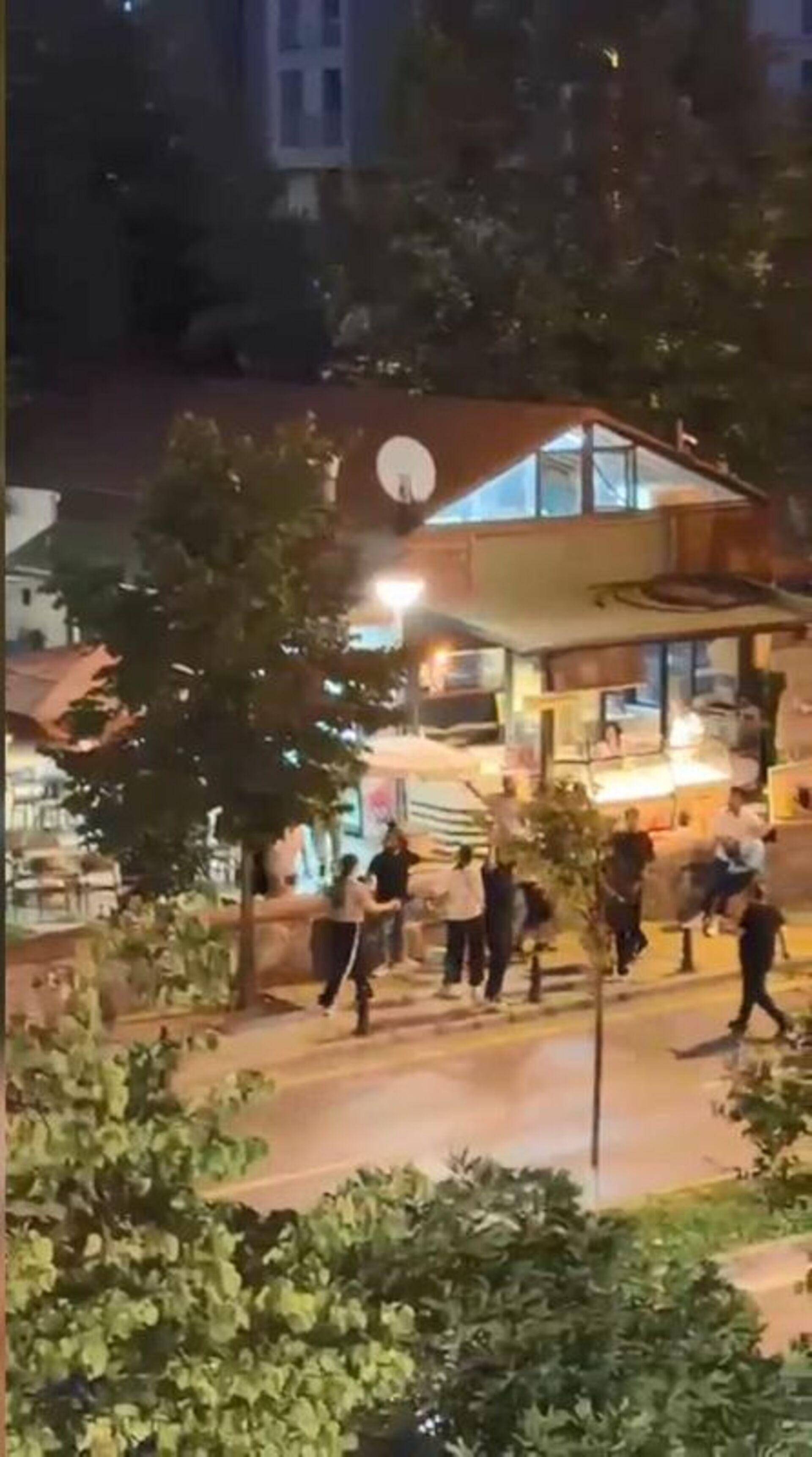 Gece saatlerinde bir sokakta toplanan kişilerin ve çevredeki binaların görüntüsü.