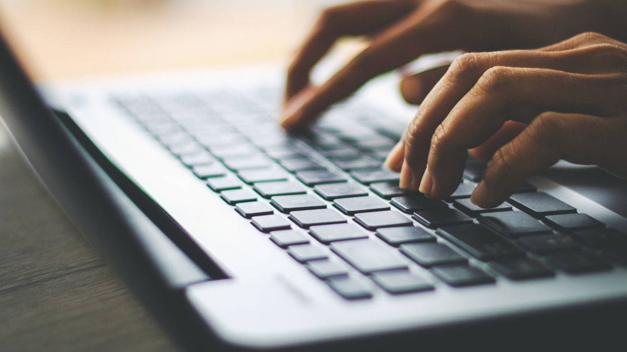 Hands of a person typing on a laptop keyboard.