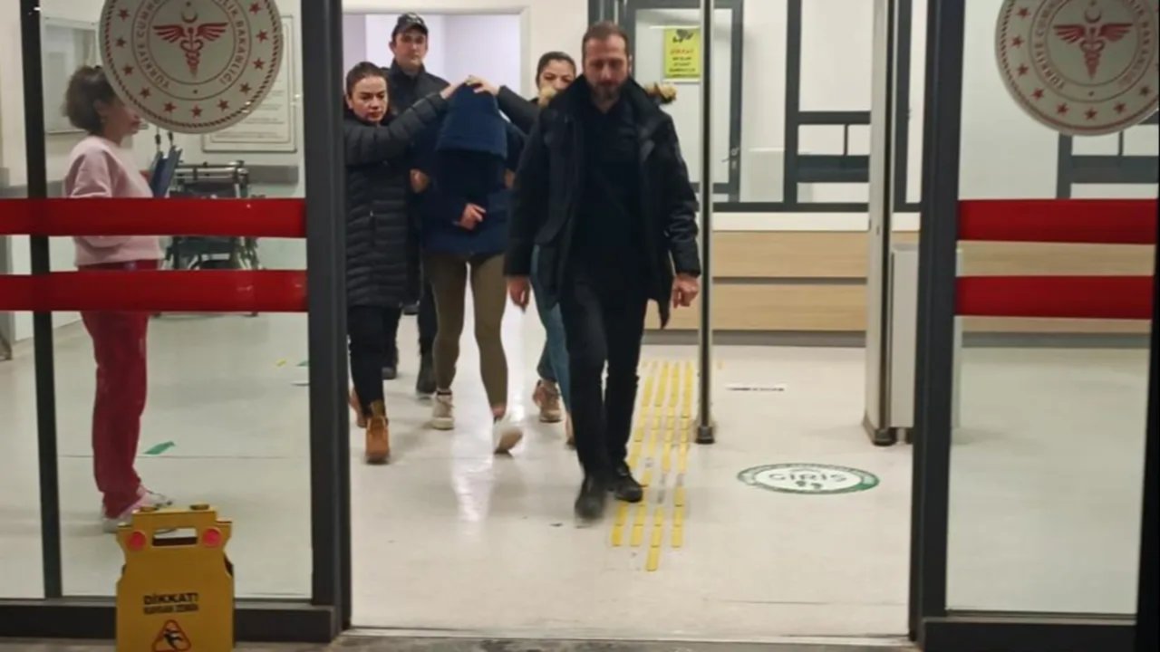 Bir sağlık kurumu girişinde görevliler eşliğinde yürüyen kişilerin görüntüsü.