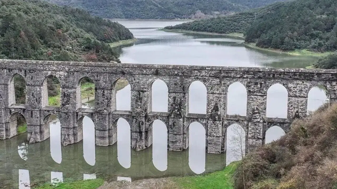 Ormanlık alanlar arasında yer alan bir baraj havzası ve tarihi su kemeri görünümü.