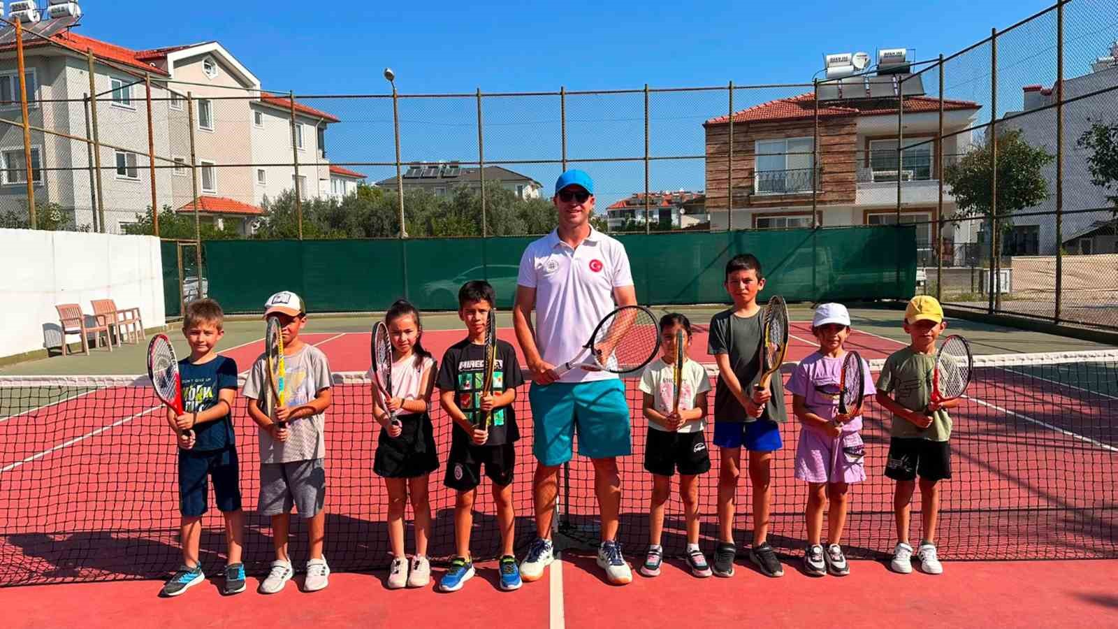 Tenis kortunda eğitmenle birlikte raketleriyle poz veren çocuklar.