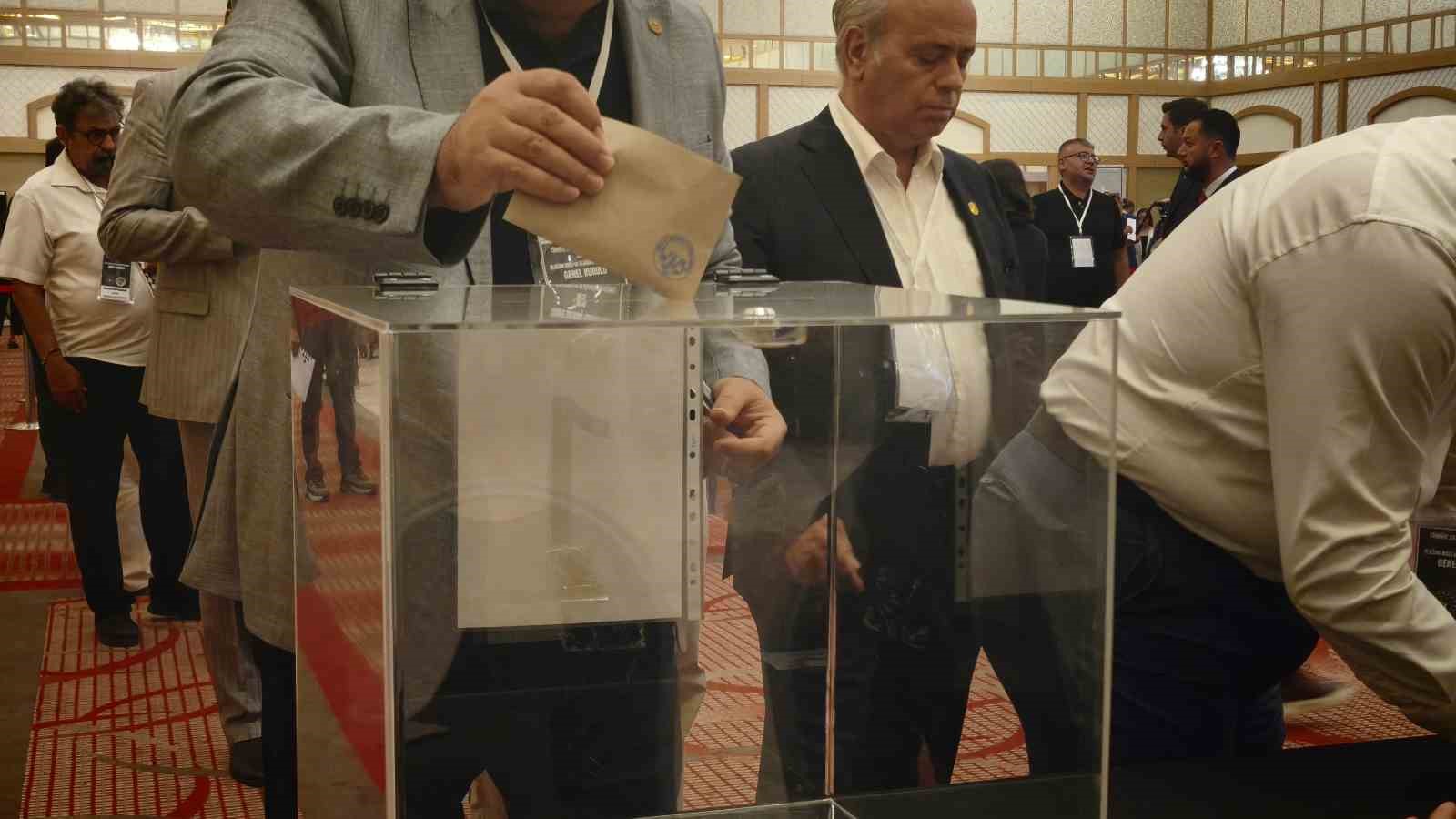Bir delegenin şeffaf sandığa oy zarfı attığı genel kurul görüntüsü.