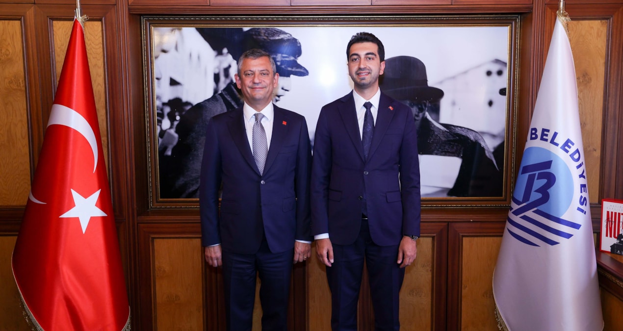 Özgür Özel ve Eren Ali Bingöl, belediye makamında Türk bayrağı ve belediye flaması önünde yan yana duruyor.