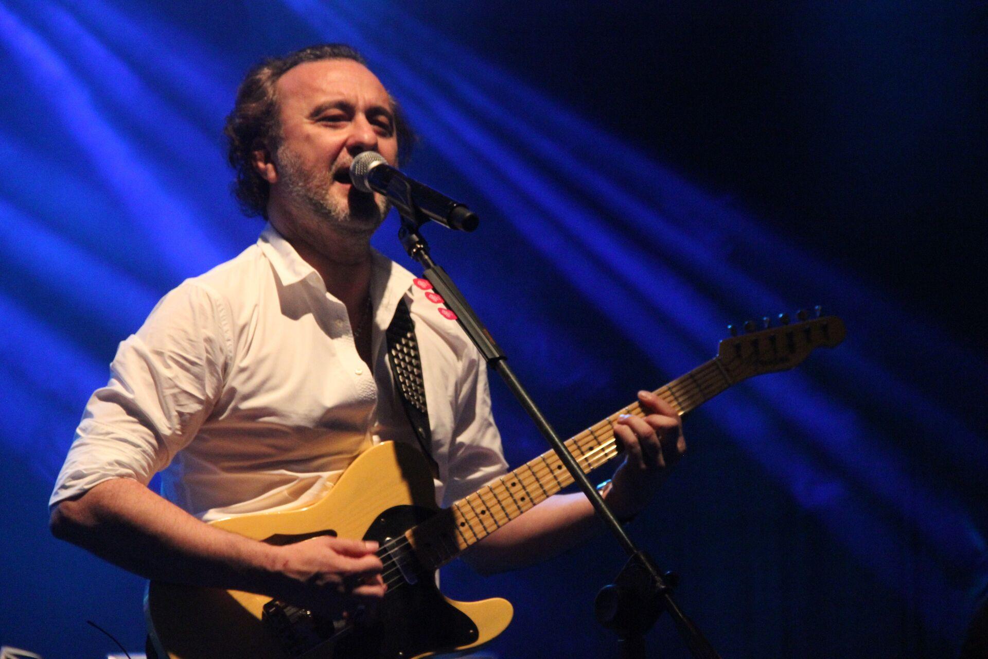 Le chanteur Nev est vu sur scène en train de jouer de la guitare et de chanter devant un micro.